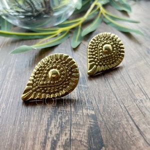 Op de afbeelding: Een paar gouden oorringen in de vorm van een traan met een textuur en parelmoer.