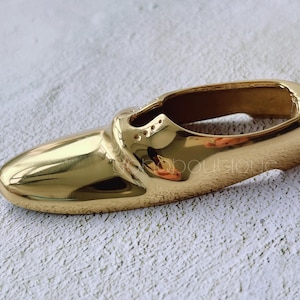 Pode incluir: Um porta-anéis de metal dourado em forma de sapato. O porta-anéis é liso e brilhante.