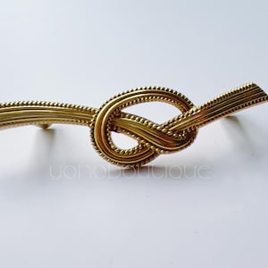 May include: A gold-toned metal cabinet pull with a knotted design. The pull is shaped like a rope with a knot in the center.