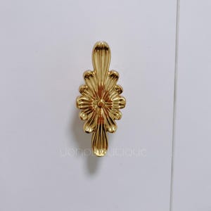 Op de afbeelding: Een gouden metalen kastknop met een decoratief bloemmotief.