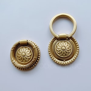 May include: Two gold-toned cabinet knobs with ornate floral designs. The larger knob has a ring handle and the smaller knob has a round handle.