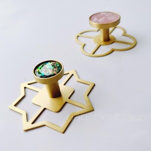 May include: Two gold metal hooks with geometric designs. One hook has a pink iridescent stone and the other has a green iridescent stone.