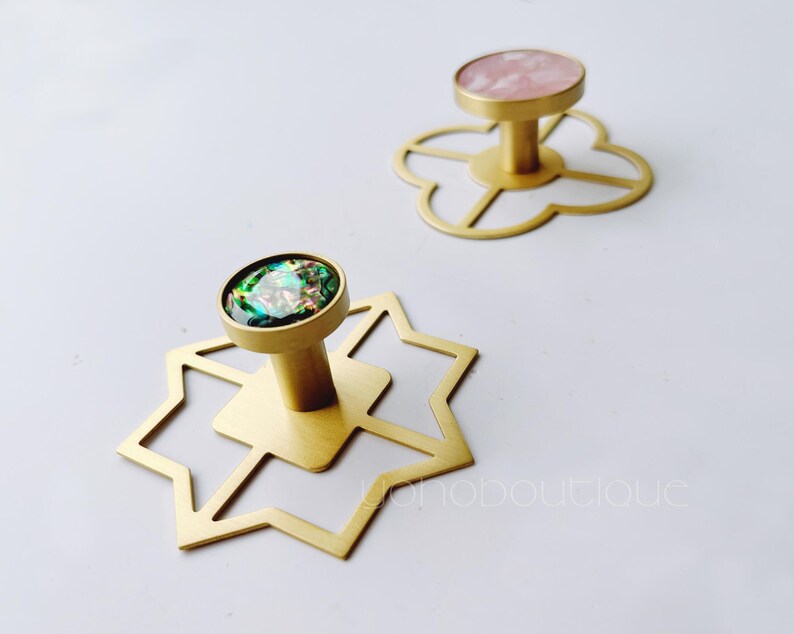 May include: Two gold metal hooks with geometric designs. One hook has a pink iridescent stone and the other has a green iridescent stone.