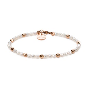 May include: A delicate bracelet with a personalized charm that reads "Lina". The bracelet is made of white pearls and gold beads.