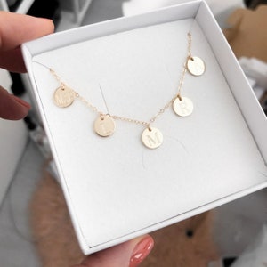 May include: A gold necklace with five small round charms, each with a letter engraved on it. The letters spell out "MARIL." The necklace is displayed in a white box.
