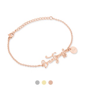 May include: Rose gold bracelet with the name "Brautjungfer" in a cursive font. A small, round charm with the name "Lina" is attached. The bracelet has an adjustable chain and a lobster clasp.