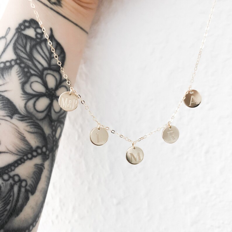 May include: Gold chain necklace with five round charms, each engraved with a letter. The charms spell out "MARL" and "M&P".
