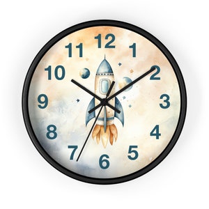 May include: A black framed clock with a watercolor background of clouds and stars. The clock face features a rocket ship with a blue and white design and orange flames. The numbers on the clock face are in blue.