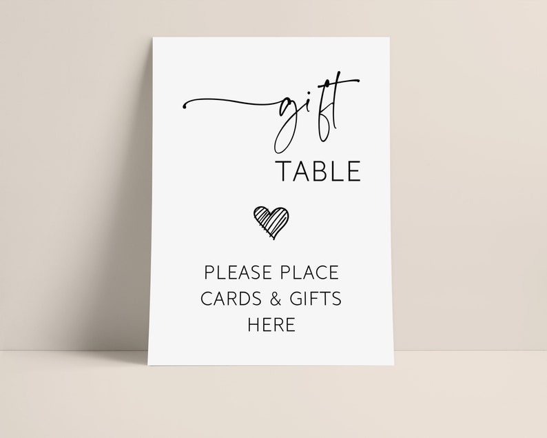 May include: A white sign with black text that reads "gift table" with a small heart symbol below. The text below the heart reads "Please place cards & gifts here".