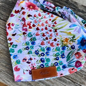May include: A white bandana with a floral print featuring colorful flowers and green leaves. The bandana has a brown leather tag with the word "Willow" printed on it.