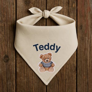 May include: Beige bandana with a navy blue embroidered teddy bear and the name "Teddy" in navy blue.