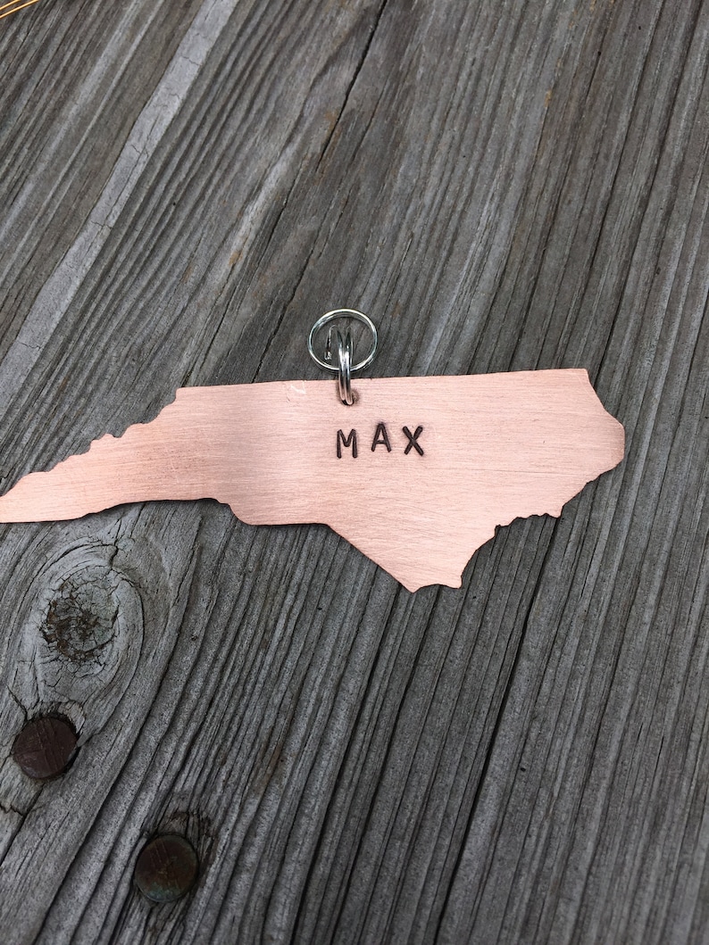 K&ouml;nnte beinhalten: Ein kupferfarbener Anh&auml;nger in Form des Bundesstaates North Carolina mit einem silbernen Schl&uuml;sselring. Der Anh&auml;nger tr&auml;gt den eingravierten Namen "MAX".