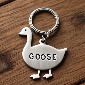 May include: A silver goose keychain with a key ring and the word "GOOSE" engraved on the goose's body.