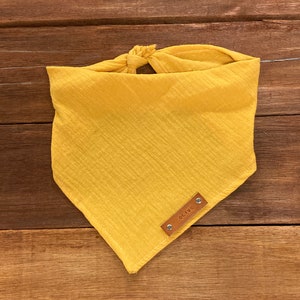 May include: A yellow cotton bandana with a brown leather tag that says "OLIVE".