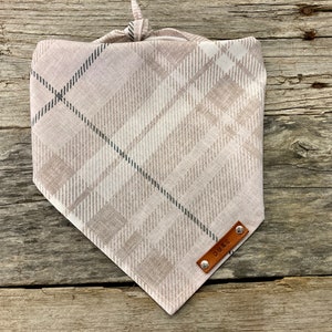May include: A beige and gray plaid dog bandana with a brown leather tag that says "Duke".