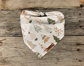 May include: White cotton dog bandana with a brown leather tag that says "Duke". The bandana has a pattern of stylized green, brown, and beige trees.