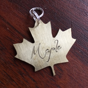 May include: A gold-colored maple leaf keychain with the word "Maple" engraved on it.