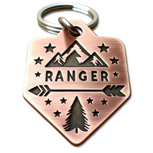 May include: Copper dog tag with a mountain range, a pine tree, and an arrow with the word "RANGER" engraved in black.