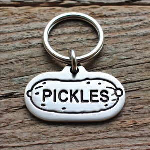 May include: Silver key chain with a pickle-shaped tag that says "PICKLES" in black lettering.