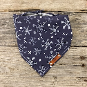 May include: A navy blue bandana with a white snowflake pattern and a brown leather tag that says "Duke".