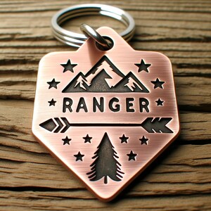 May include: Copper-colored key chain with a mountain range design, a pine tree, an arrow, and the word "RANGER" in black lettering. The key chain is surrounded by small stars.