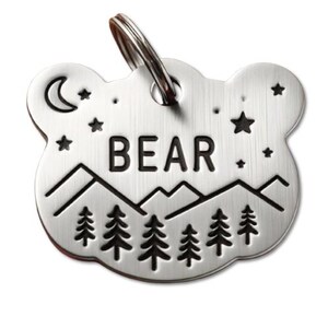 May include: Silver bear-shaped dog tag with a black mountain range, trees, and stars design. The tag says "BEAR" in black lettering.