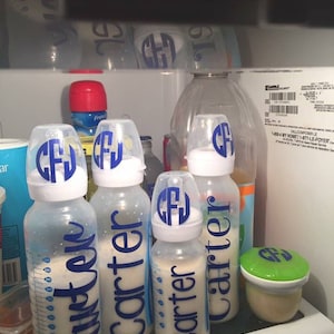 Peut inclure: Quatre biberons en verre transparent avec des &eacute;tiquettes bleues et blanches indiquant "Carter" et "Just Like" dans un r&eacute;frig&eacute;rateur. Les biberons sont remplis d'un liquide blanc. Il y a un r&eacute;cipient vert avec un couvercle dans le coin inf&eacute;rieur droit.