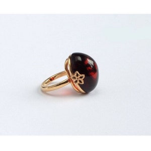 May include: A gold ring with a large, dark red oval-shaped gemstone. The ring has a delicate floral design on the band.