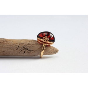 May include: A gold ring with a large, dark red, semi-circular amber stone set in a gold filigree design.