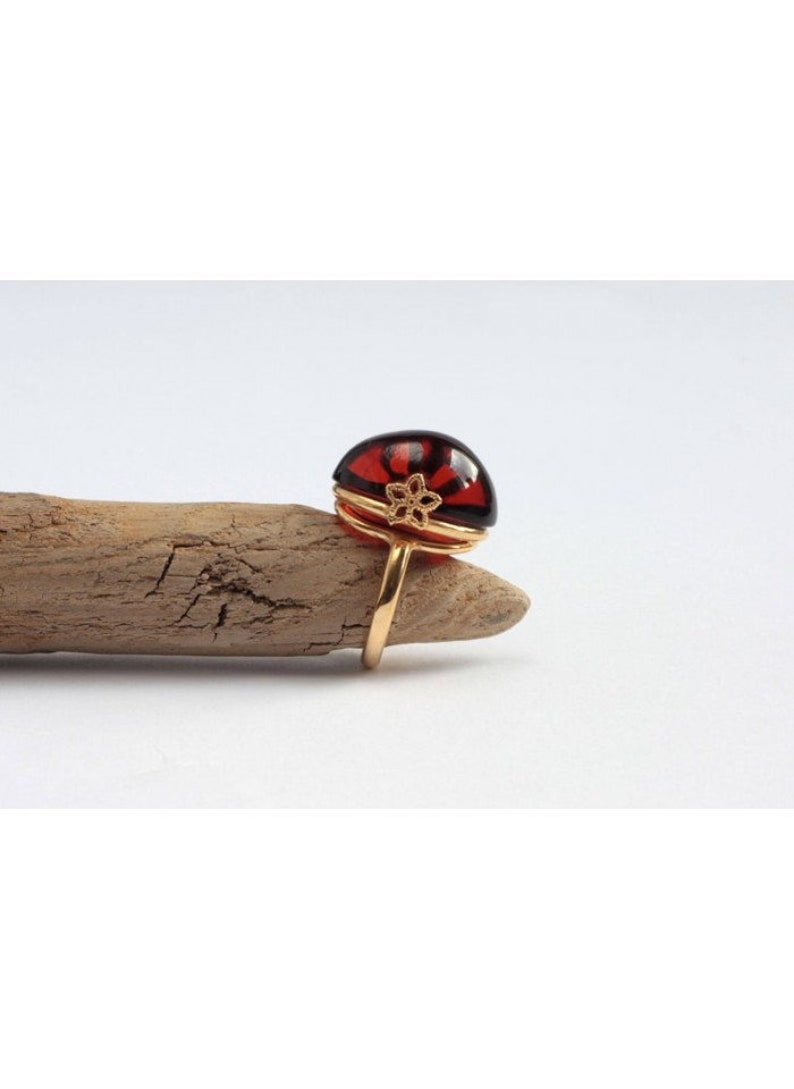 May include: A gold ring with a large, dark red, semi-circular amber stone set in a gold filigree design.