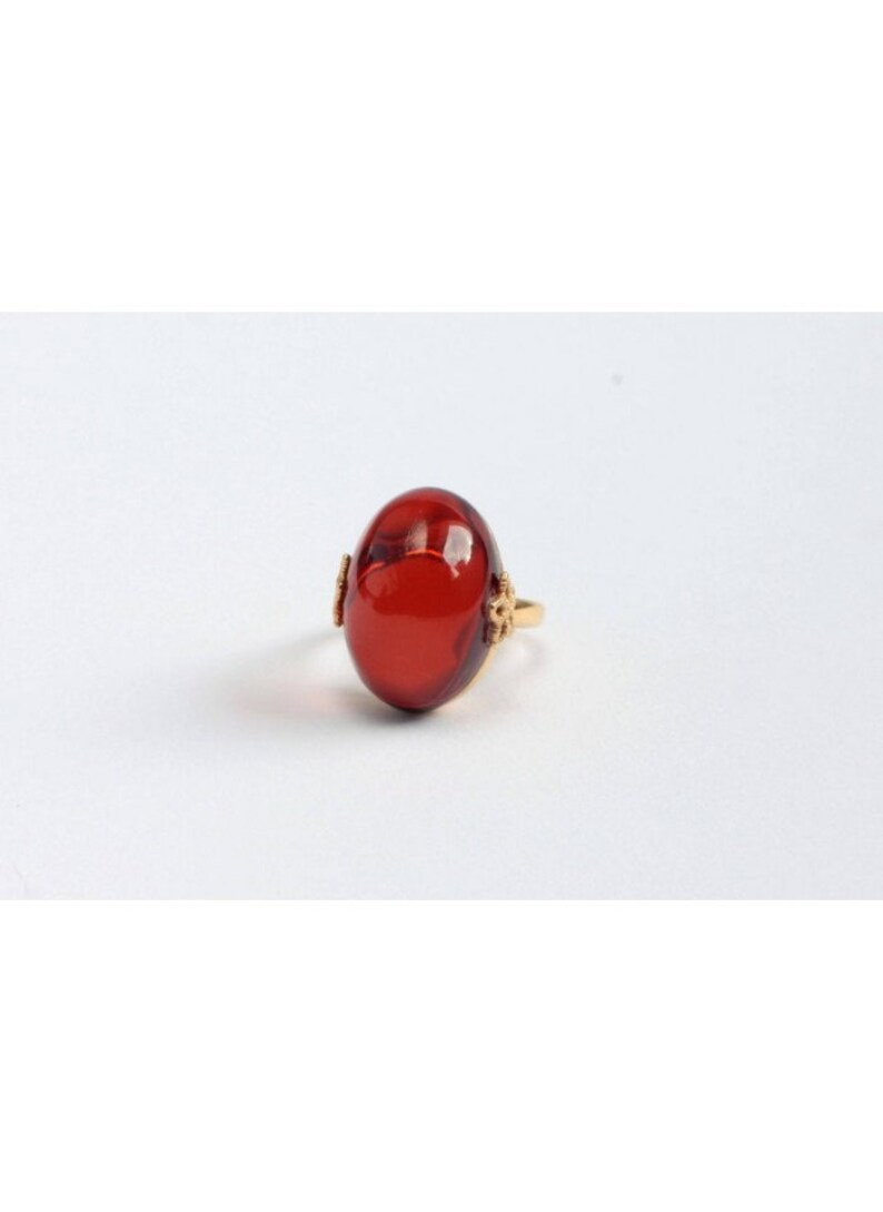 May include: A gold ring with a large, oval-shaped, red gemstone.