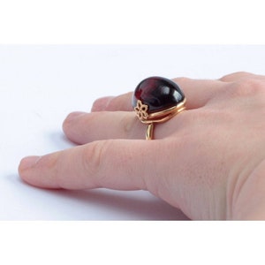 May include: A gold ring with a large, dark red oval gemstone. The ring has a delicate floral design on the band.