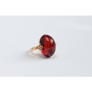May include: A gold ring with a large, oval-shaped, red gemstone.