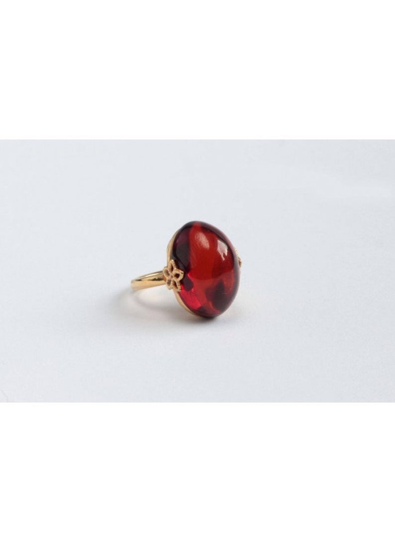 May include: A gold ring with a large, oval-shaped, red gemstone.