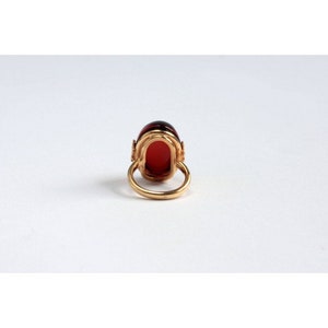May include: A gold ring with a large, oval-shaped red gemstone set in a gold setting. The ring is on a white background.