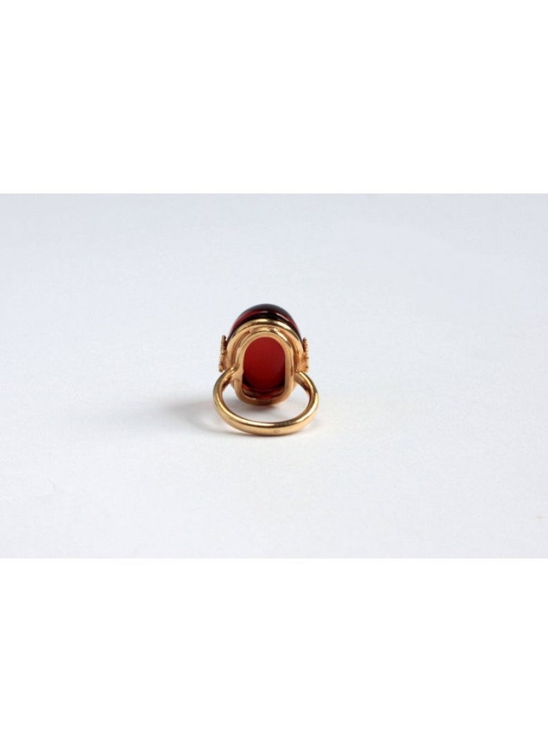 May include: A gold ring with a large, oval-shaped red gemstone set in a gold setting. The ring is on a white background.