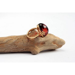 May include: A gold ring with a large, round, red amber stone. The ring has a delicate floral design on the band.