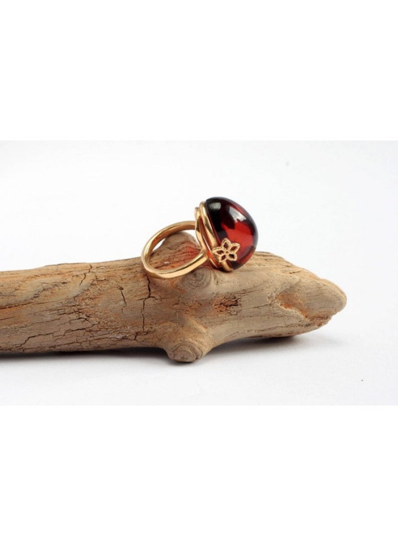May include: A gold ring with a large, round, red amber stone. The ring has a delicate floral design on the band.