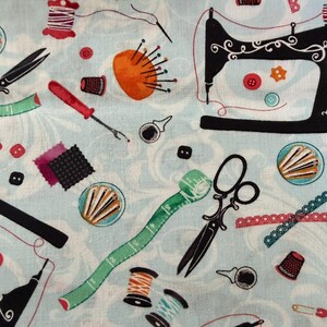 May include: Light blue fabric with a pattern of sewing tools. The design includes a black sewing machine, scissors, spools of thread, buttons, a pin cushion, and a measuring tape. The fabric has a floral design.