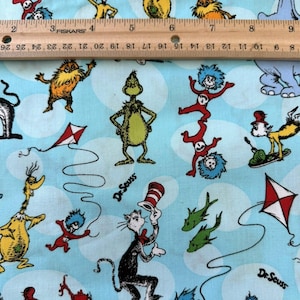 May include: Pale blue fabric with Dr. Seuss characters including the Cat in the Hat, the Grinch, and Thing 1 and Thing 2. White cloud shapes and the text "Dr. Seuss" are visible. A ruler is placed across the top of the fabric.