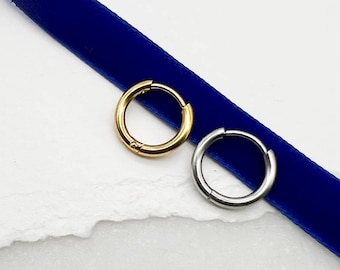 Può includere: Due orecchini a cerchio, uno dorato e uno argentato, su un nastro di velluto blu. Il testo "Moon Dance" è scritto sotto gli orecchini.
