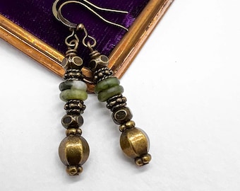 Può includere: Orecchini fatti a mano con un design vintage. Gli orecchini presentano una combinazione di perline in metallo color ottone, perline di pietra verde e elementi decorativi. Il testo "Moon Dance Crafted" è visibile sullo sfondo.