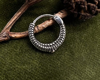 Può includere: Orecchino a cerchio color argento con un design a pois strutturato. L'orecchino è posto su uno sfondo verde, con un rametto e una pigna. Le parole "Moon Dance" sono visibili nell'angolo in basso a destra.