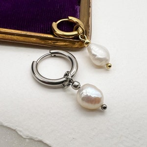 Könnte beinhalten: Ein Paar Ohrringe mit einem Perlenanhänger. Ein Ohrring hat einen goldenen Ring und der andere einen silbernen Ring. Die Ohrringe liegen auf einer weißen Oberfläche mit dem Text "Moon Dance" darunter.