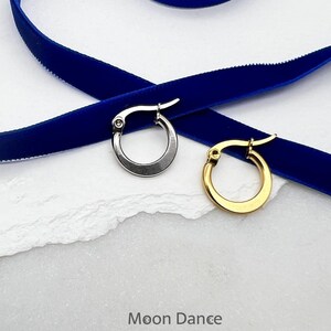 Könnte beinhalten: Zwei Creolen, eine silberne und eine goldene, auf einem blauen Samtband. Der Text "Moon Dance" ist unter den Ohrringen gedruckt.