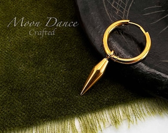 Può includere: Orecchino a cerchio dorato con un ciondolo a forma di cono. L'orecchino è mostrato su un tessuto verde scuro e una superficie nera strutturata. Il testo "Moon Dance Crafted" è visibile.