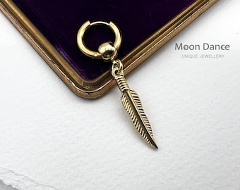 Può includere: Orecchino a cerchio dorato con ciondolo a forma di piuma. L'orecchino è su uno sfondo di velluto viola. Moon Dance Gioielli Unici.
