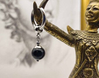 May include: A silver hoop earring with a black gemstone dangling from it. The earring is displayed on a golden statue.