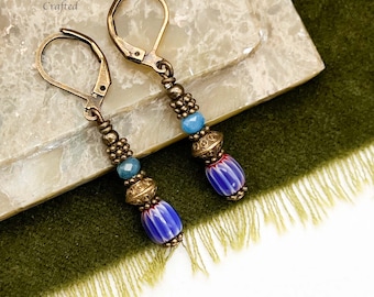 Può includere: Orecchini fatti a mano con chiusura a leva. Gli orecchini presentano perline blu, oro e rosse. Il testo "Moon Dance Crafted" è visibile nell'angolo in alto a sinistra.