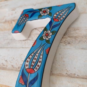 Peut inclure: Un numéro de maison en céramique bleu et blanc avec un motif floral. Le numéro est peint avec un motif turc traditionnel avec des fleurs rouges, blanches et bleues.